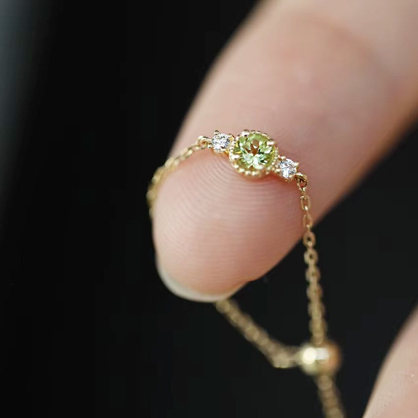 En närbild av en 14K guldpläterad 925 sterling silver justerbar kedjering, med en livlig grön olivine zirkonia födelsesten.