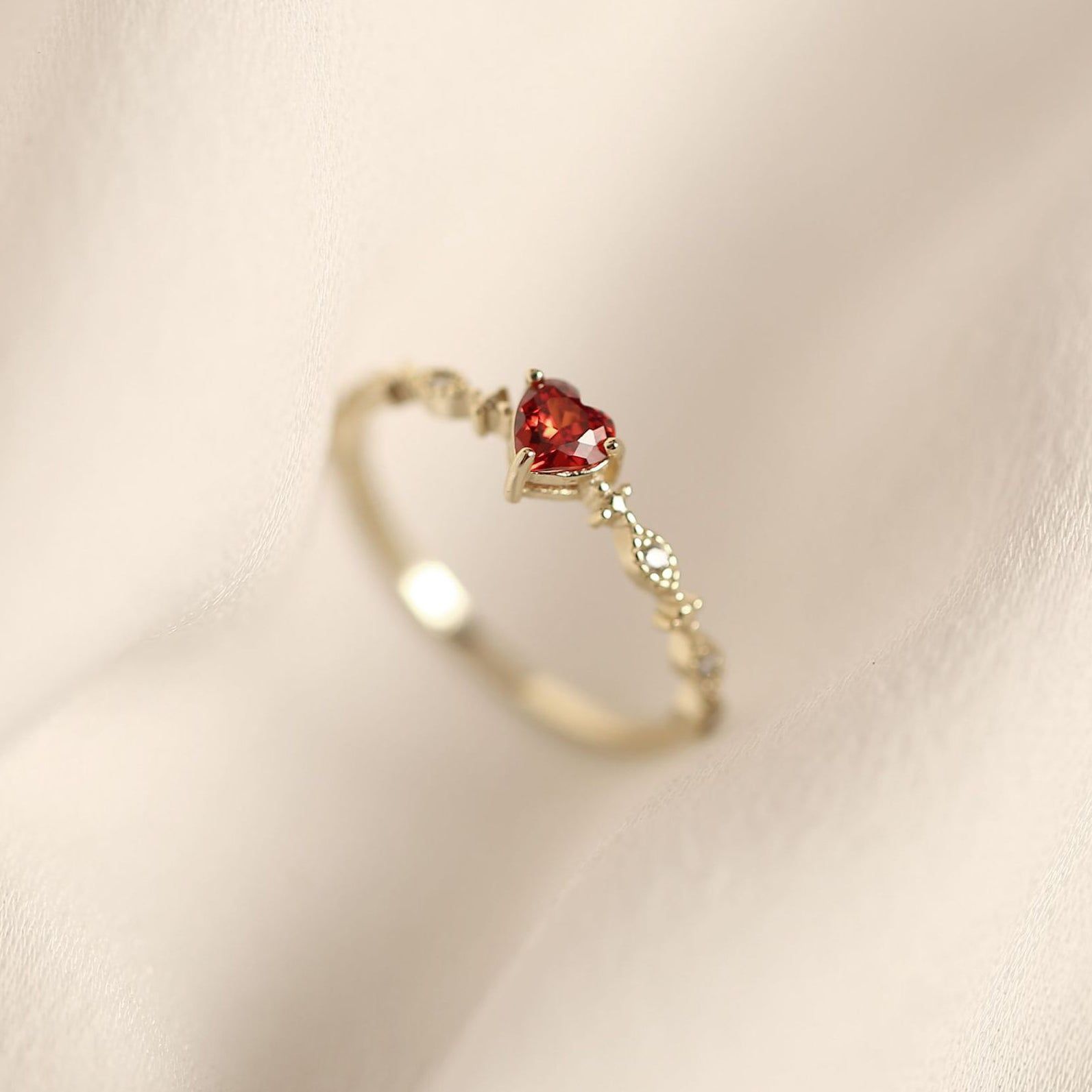 Gros plan d'une bague en argent sterling 925 avec finition dorée, présentant un brillant rubis rouge en forme de cœur au centre, de JR Fashion Accessories.