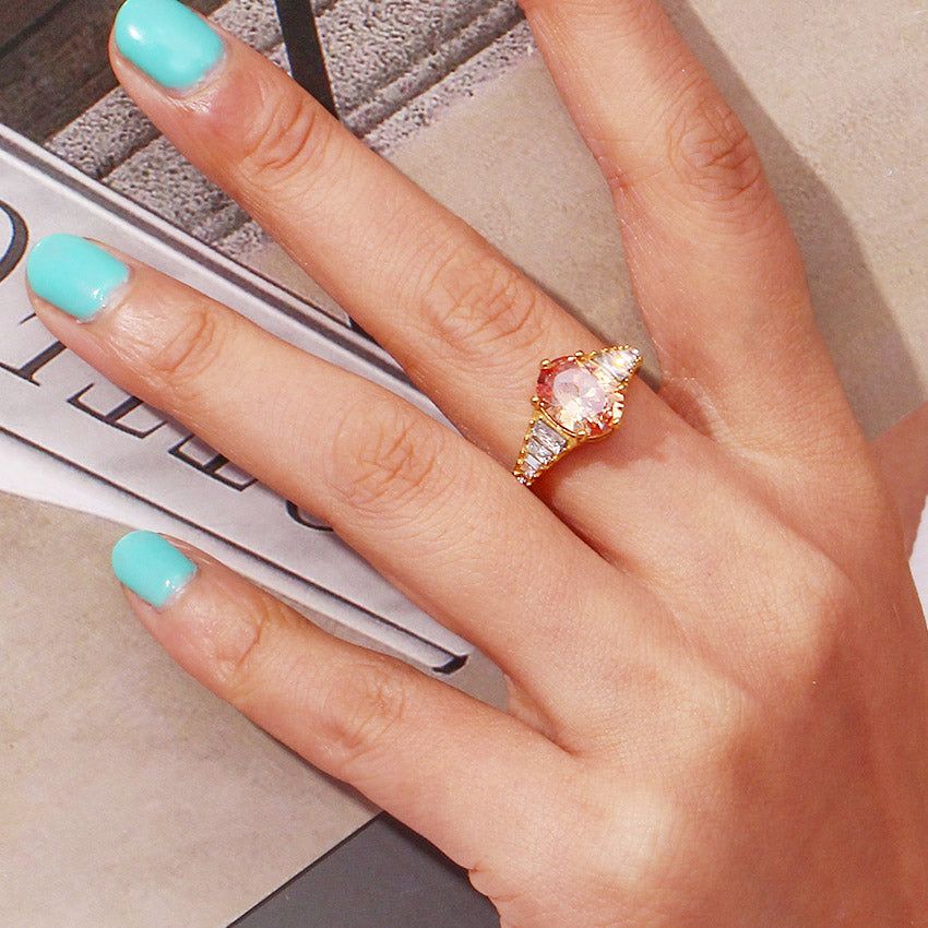 Un primo piano dell'anello regolabile in zirconia ovale in acciaio inossidabile con finitura oro champagne, che mostra la grande pietra centrale e gli accenti laterali.