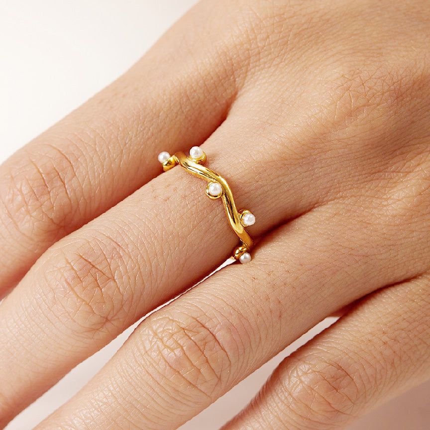 A mão de uma mulher usando o anel de aço inoxidável banhado a ouro com detalhes em pérola do conjunto de 5 peças.