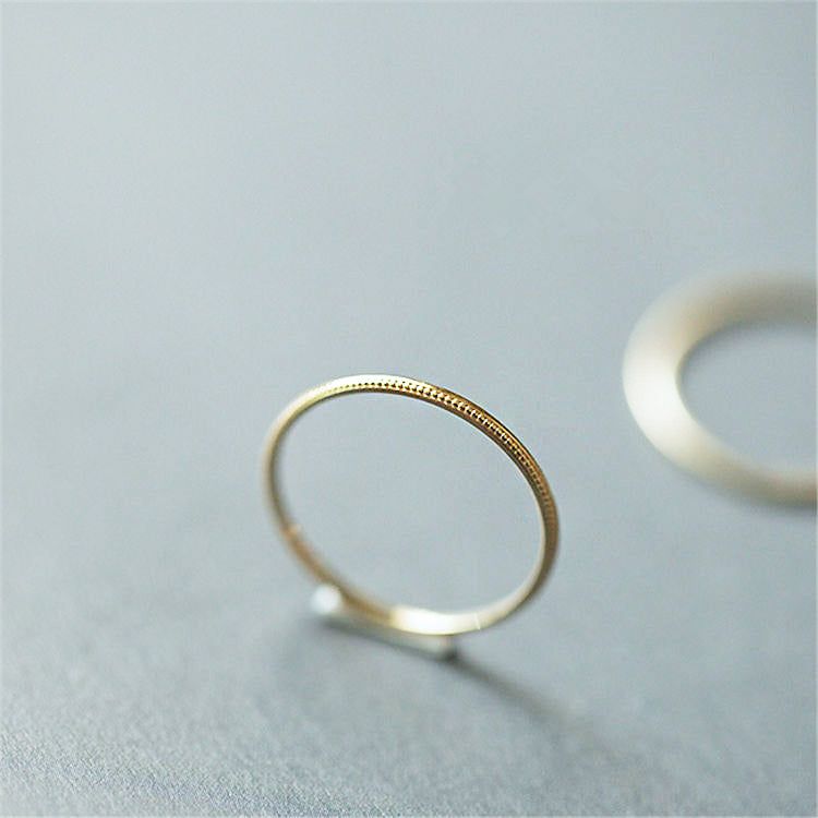 Une bague empilable minimaliste en argent sterling 925 avec une finition en or texturé, montrée sur le côté pour détailler l'artisanat.