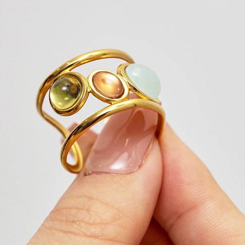 Um anel de pulso ajustável em aço inoxidável com acabamento em ouro do conjunto, apresentando três pedras vibrantes no estilo opala.