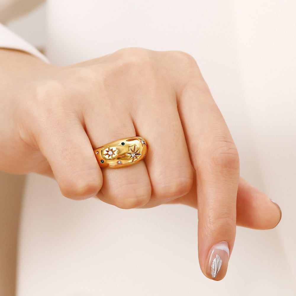 La mano de una mujer usando un anillo de estrella grueso de acero inoxidable chapado en oro con piedras preciosas coloridas.