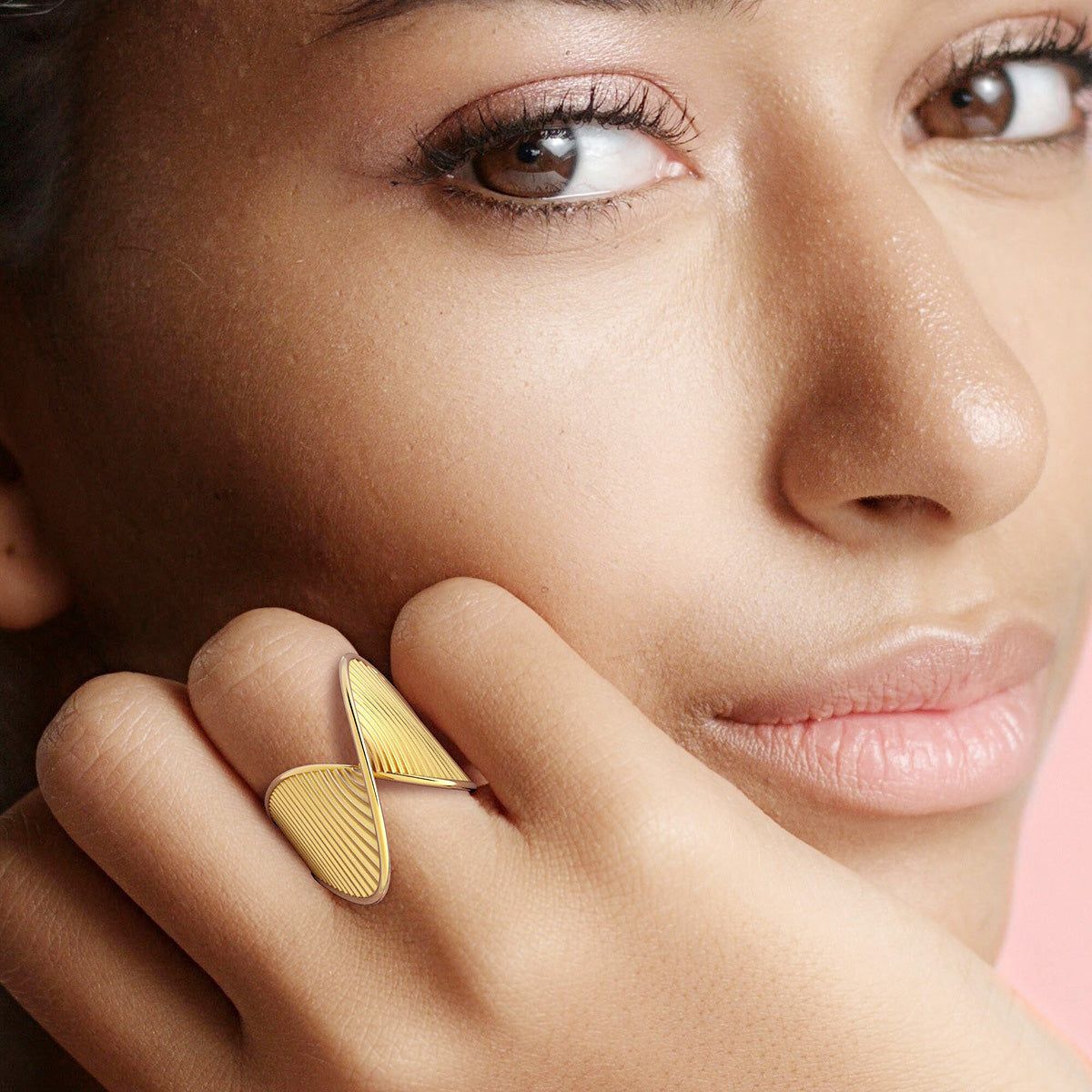 Un gros plan de la main d'une femme portant une élégante bague en acier inoxydable finition or avec un design géométrique torsadé.