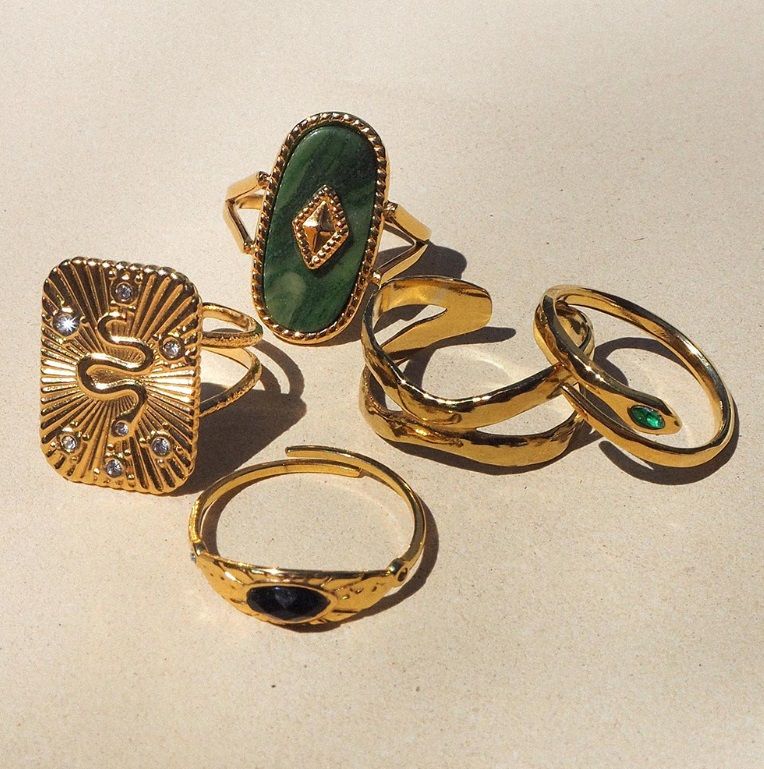 Een collectie stijlvolle roestvrijstalen 18K gouden ringen met verschillende ontwerpen, waaronder enkele met groene en zwarte edelstenen.
