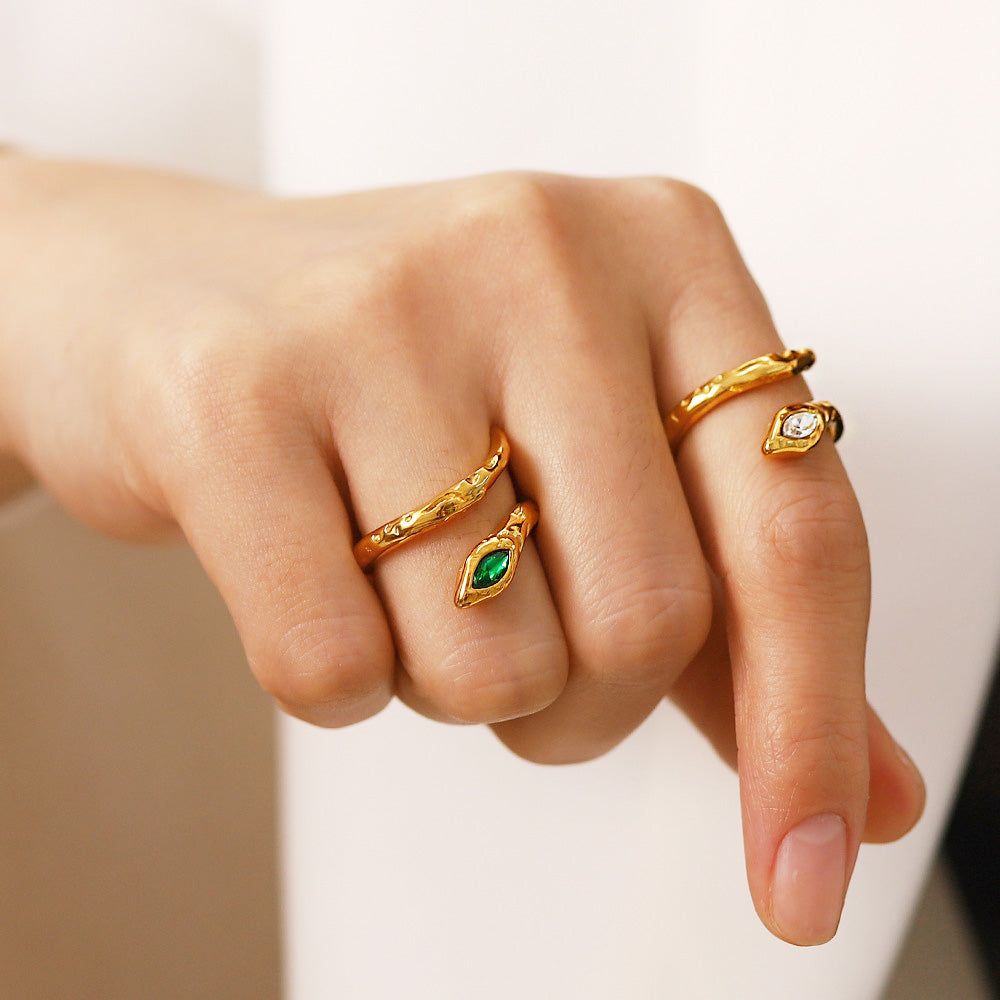La main d'un modèle portant un ensemble de quatre bagues en acier inoxydable plaqué or en forme de serpent avec des pierres de zircon blanches et vertes.