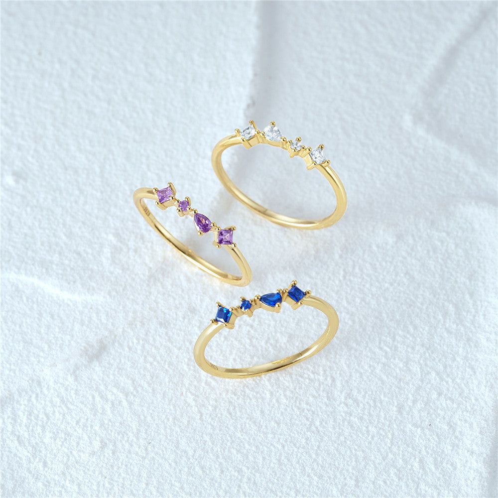 Ein Set aus drei 925 Sterling-Silber-Stapelringen in Goldoptik, jeder mit einer Reihe von vier Zirkonen in Lila, Blau und Weiß verziert.