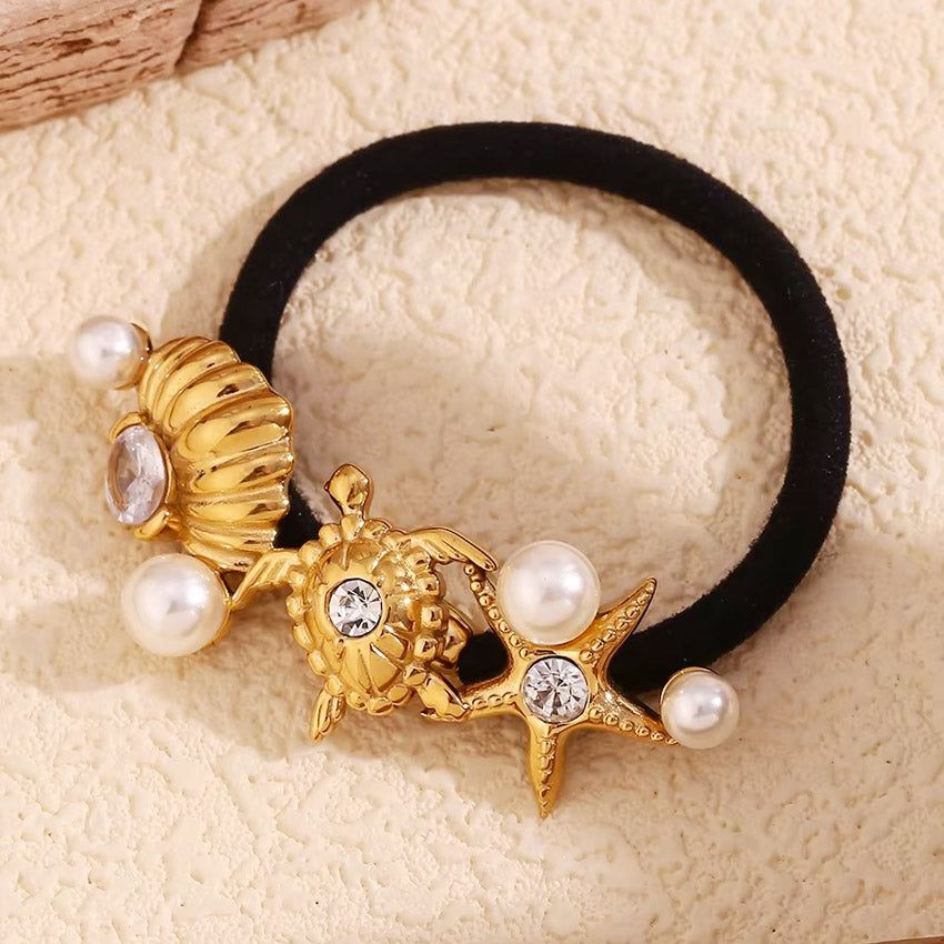 金色のヒトデチャーム、カメチャーム、光沢のあるパールで飾られたスタイリッシュな黒のヘアタイが、海をテーマにしたステンレススチールのヘアアクセサリーを披露。