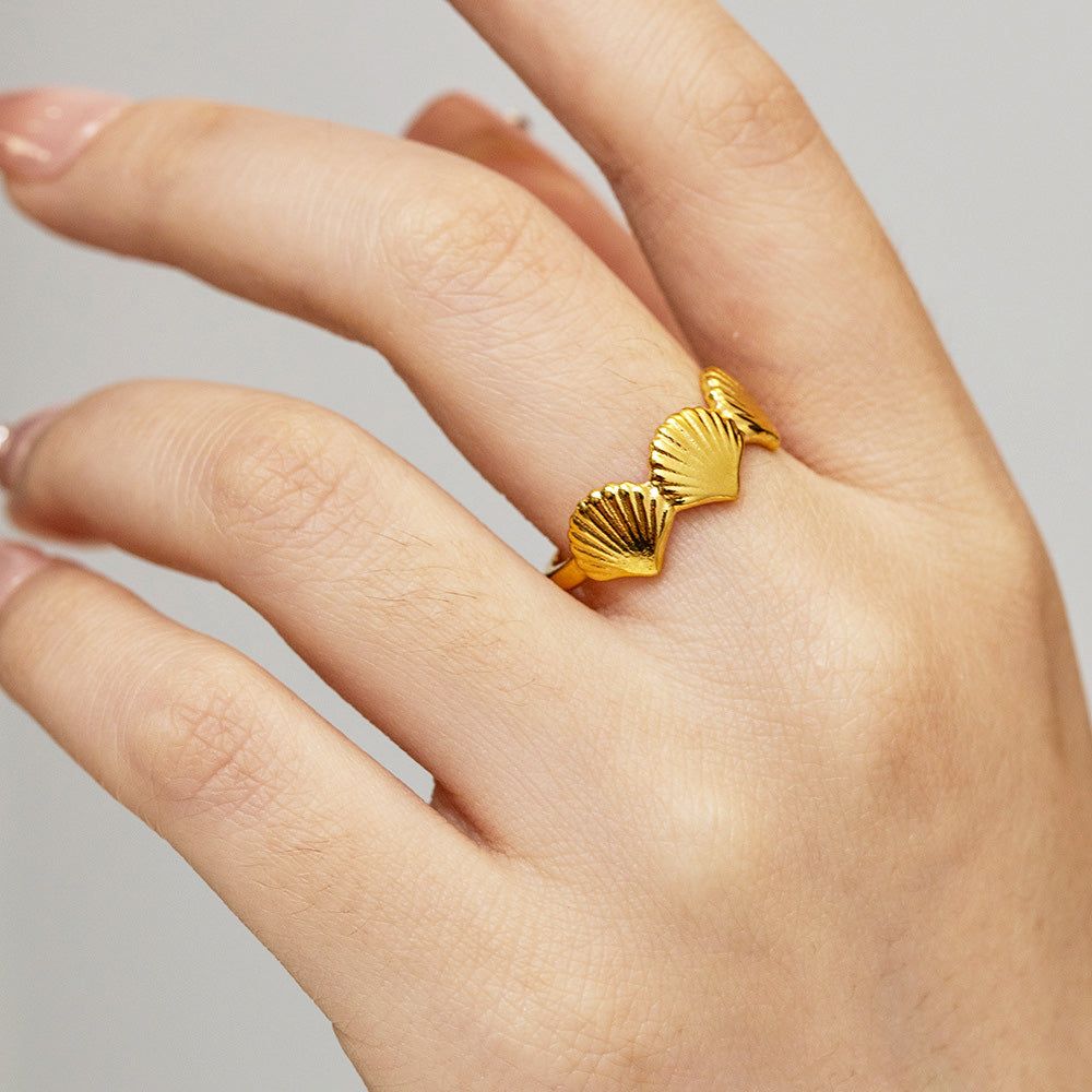 Een hand met de goudkleurige roestvrijstalen ring uit de triple shells strandjuwelen set.