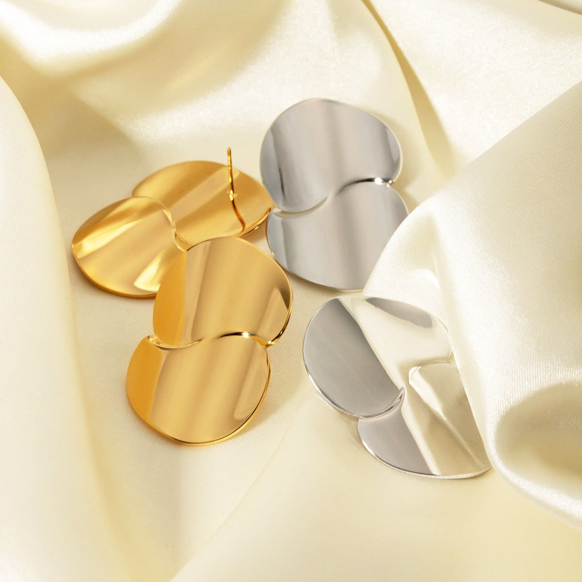 A pair of stainless steel chunky geometric drop earrings in gold and silver finishes, elegantly displayed on a satin background.