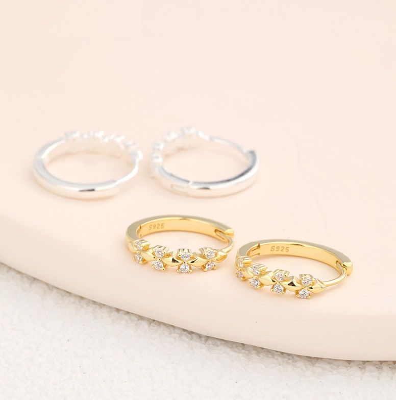 Un set di orecchini a cerchio con fiore d'oro in argento sterling 925, che mostra sia le versioni placcate in oro che in argento adornate con brillanti pietre di zirconia cubica.
