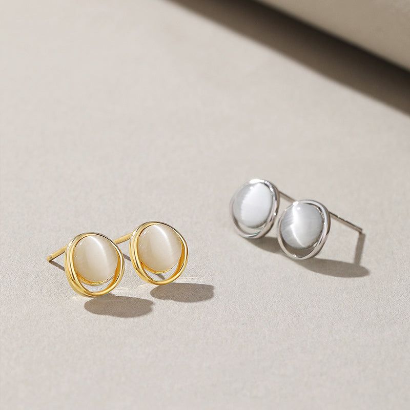 Un set elegante di orecchini a perno in argento sterling 925 con pietre a occhio di gatto bianche, esposti sia in finitura argento lucido che in oro radioso.
