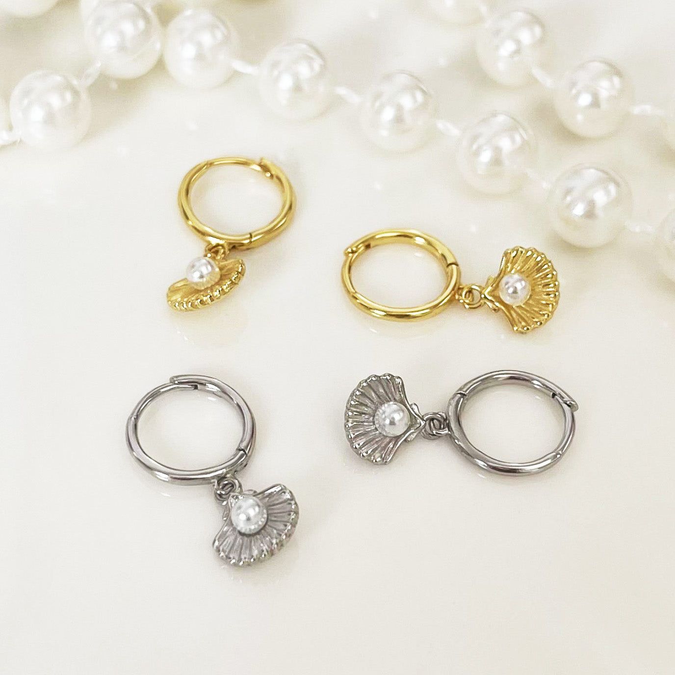 Una collezione di orecchini a cerchio huggie in argento sterling 925 con perla oceanica, esposti in finiture eleganti in oro e classico argento.