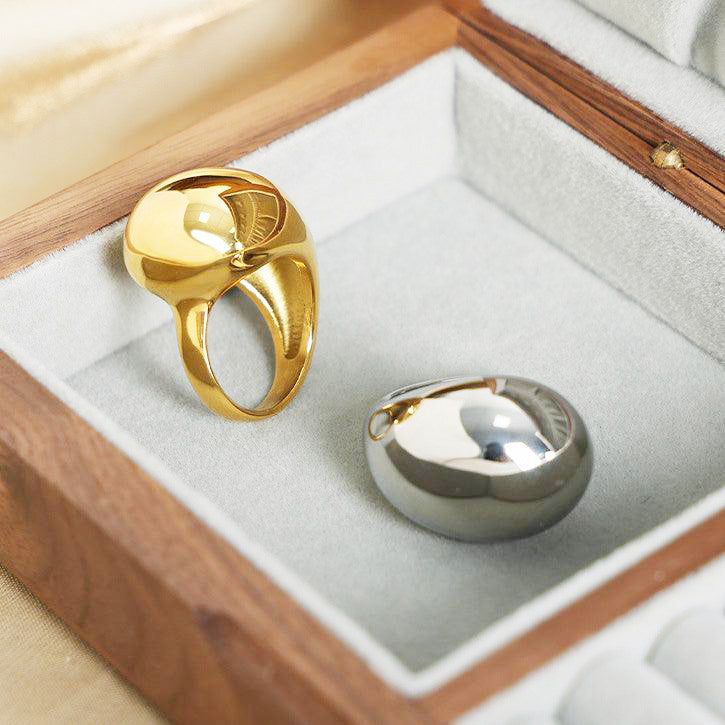 A set of stainless steel chunky drop-dripping rings in gold and silver finishes, elegantly displayed in a wooden jewelry box.