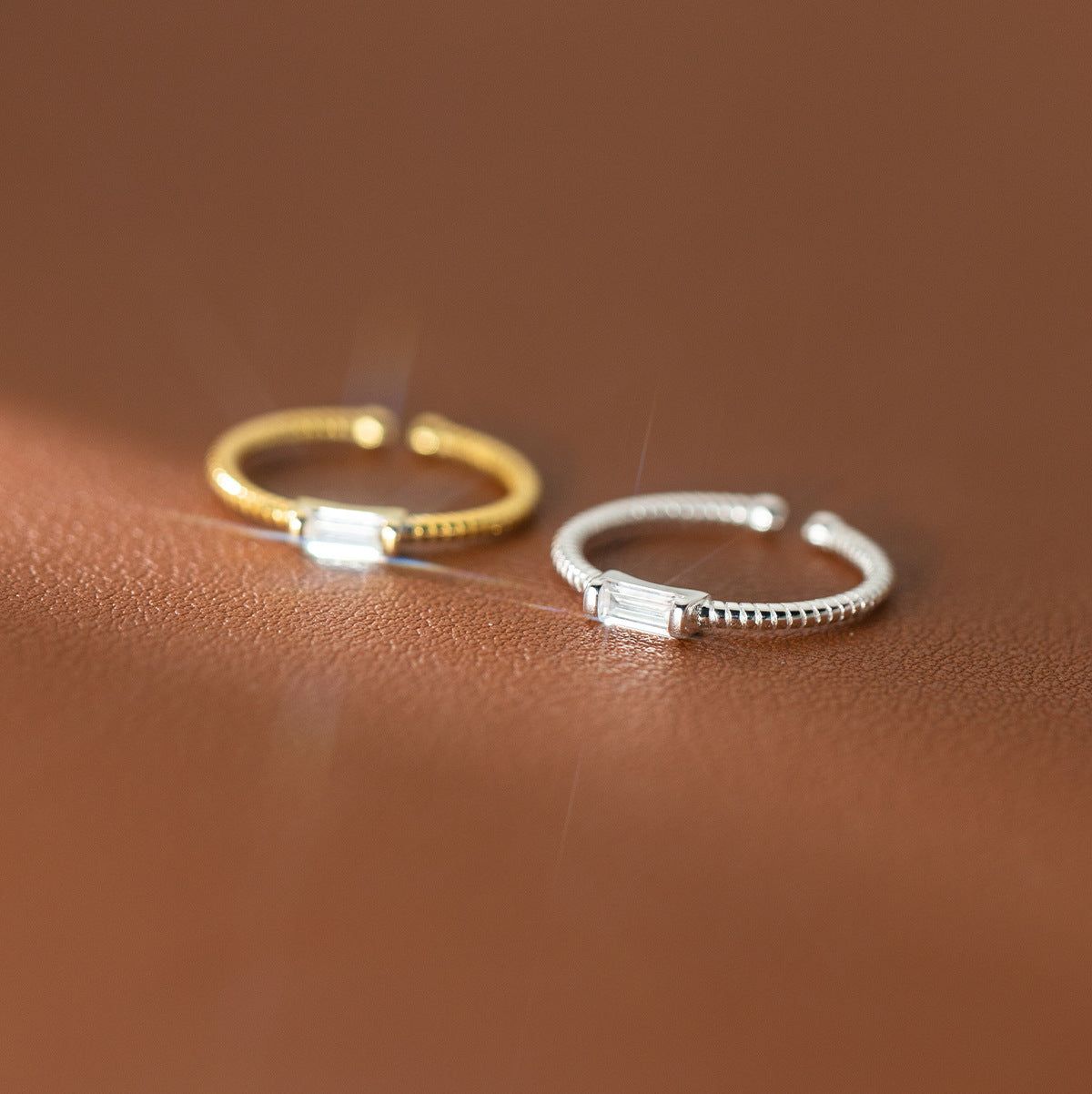 A pair of twisted rope rings in gold and silver finishes, made from 925 sterling silver, each featuring a central rectangular gemstone.