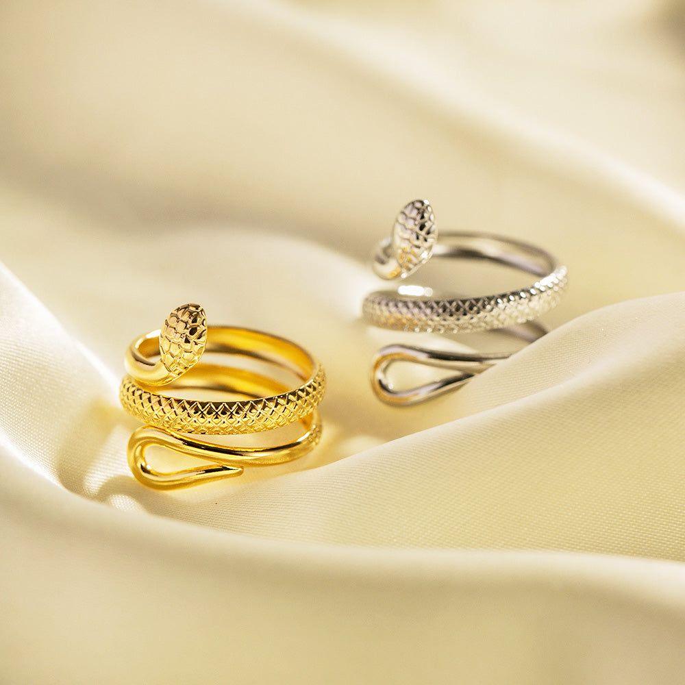 Een set van gouden en zilveren roestvrijstalen ringen met een ingewikkeld slangcurve-wikkeldesign, tentoongesteld op een luxueuze satijnen stof. Onderdeel van een krasvrije, verstelbare ringcollectie.