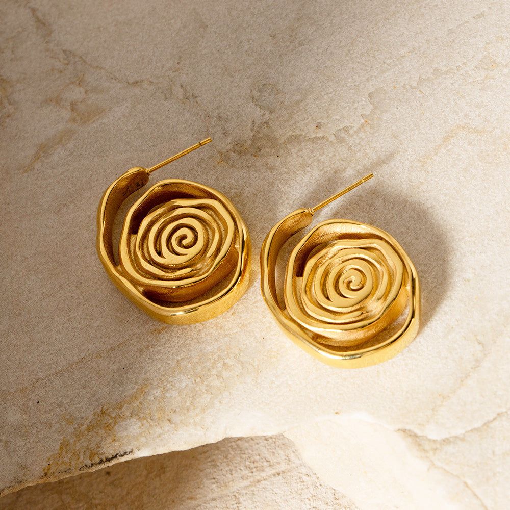 Un par de pendientes de espiral de acero inoxidable chapados en oro, impermeables y con un diseño elegante, exhibidos sobre una superficie de mármol blanco.