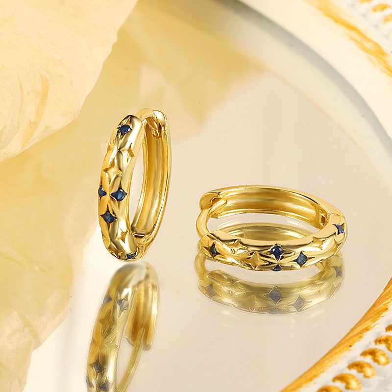 Un set di cinque orecchini huggie in argento sterling 925 con design a stella e scintillanti pietre CZ blu, esposti su uno sfondo bianco.