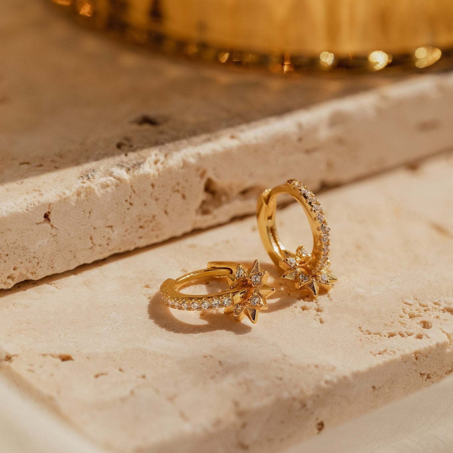 A pair of S925 gold-plated huggie earrings with removable star charms sparkling with cubic zirconia accents, presented as an ideal holiday gift.