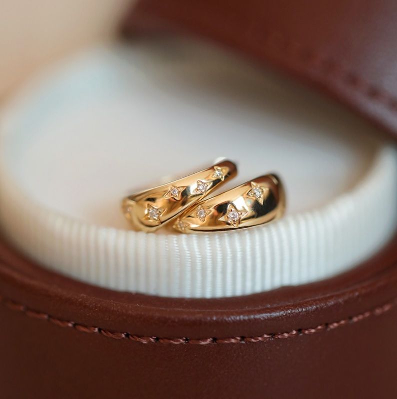 Un paio di orecchini a cerchio a stella in argento sterling 925 con placcatura in oro e zirconia cubica, elegantemente esposti in una scatola di presentazione in pelle marrone.
