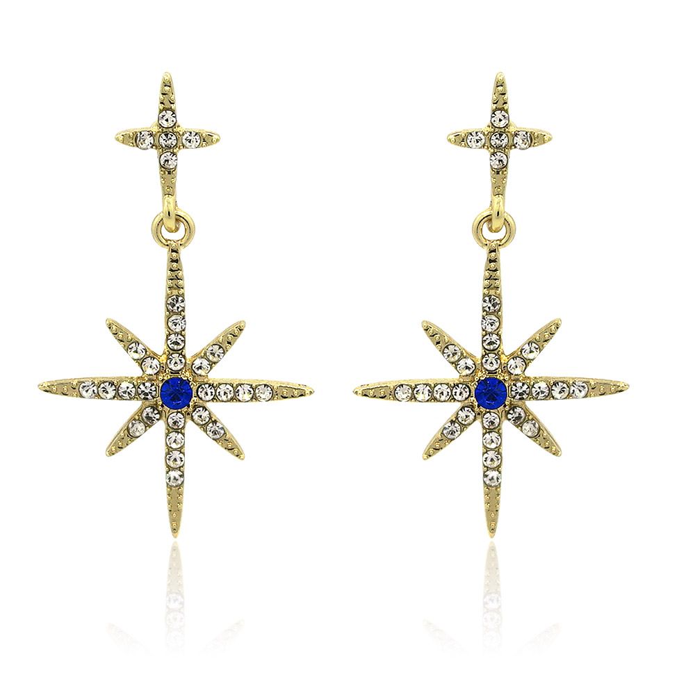 Une paire de boucles d'oreilles en forme d'étoile en cristal, avec une finition dorée et des zirconias cubiques blancs étincelants ainsi qu'une pierre centrale en verre saphir bleu.
