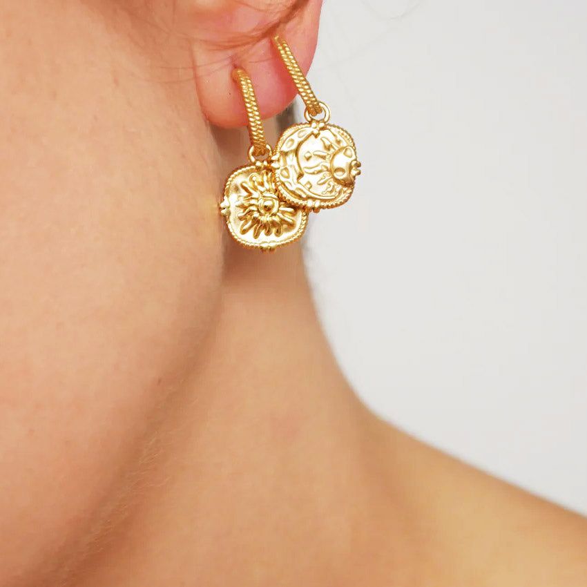 Um par de brincos pendentes de estilo vintage em aço inoxidável com revestimento em ouro PVD 18K, apresentando designs detalhados reversíveis de sol e lua crescente.