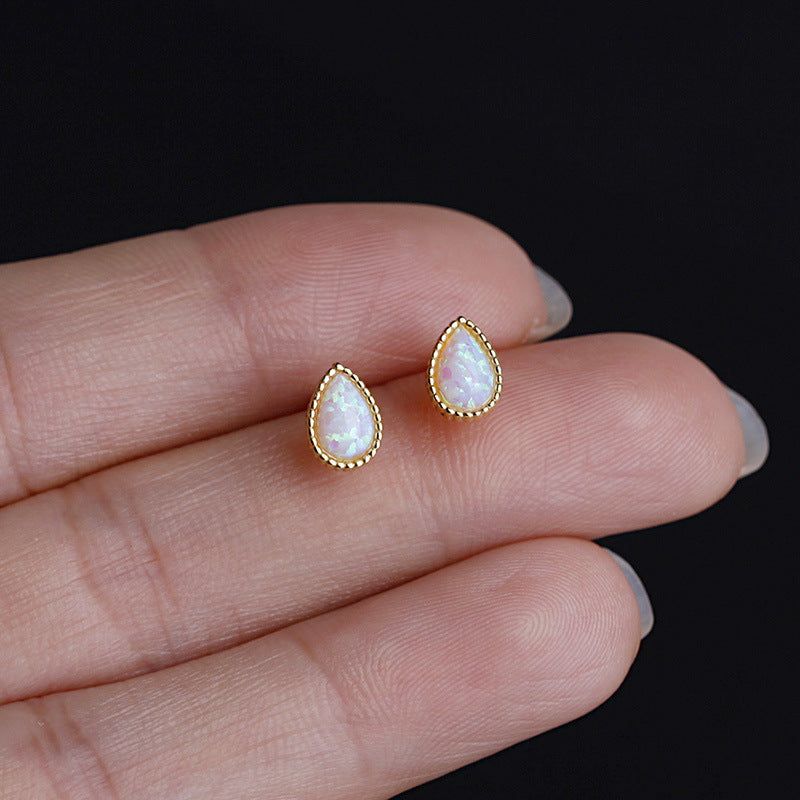 Een close-up van een paar minimalistische stud oorbellen van 925 sterling zilver, met een goudkleurig druppelontwerp en een centrale opaalsteen.