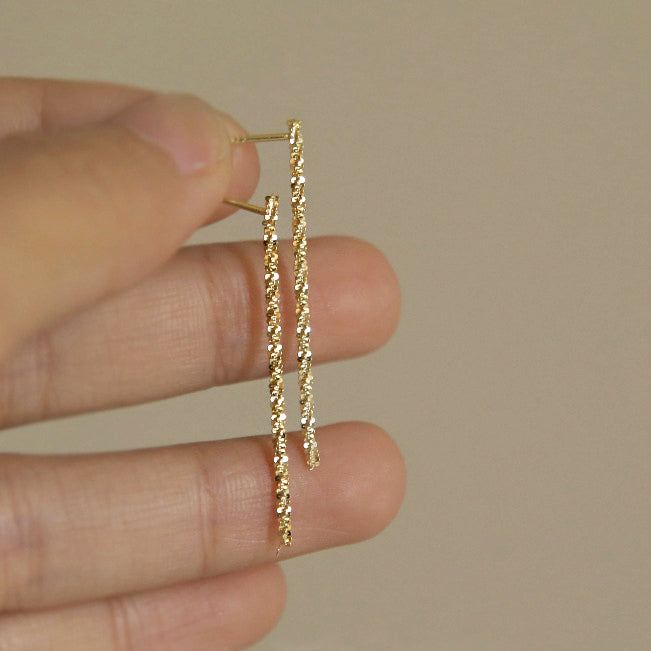 Un paio di orecchini lunghi dorati scintillanti in argento sterling 925 con un design testurizzato unico, esposti su uno sfondo bianco.