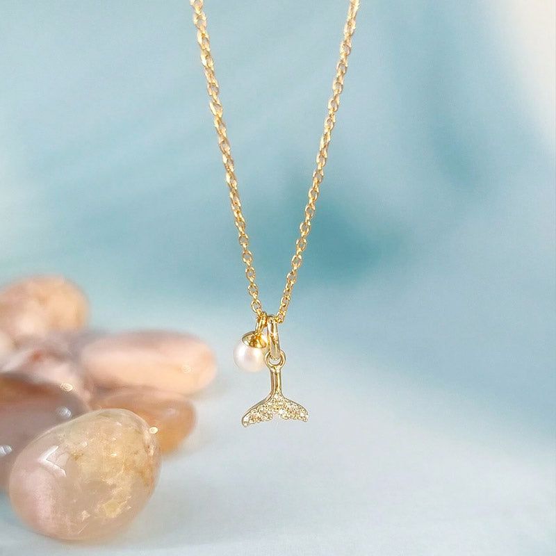 Un primo piano della collana con pendente a forma di coda di balena in argento sterling 925 con zirconia, che mette in risalto l'elegante accento di perla e i cristalli scintillanti sulla catena color oro.