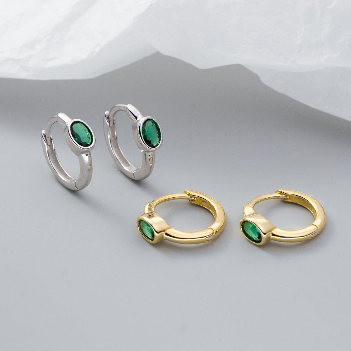 A collection of 925 sterling silver huggie hoop earrings with green oval gemstones, shown in both silver and gold plating.