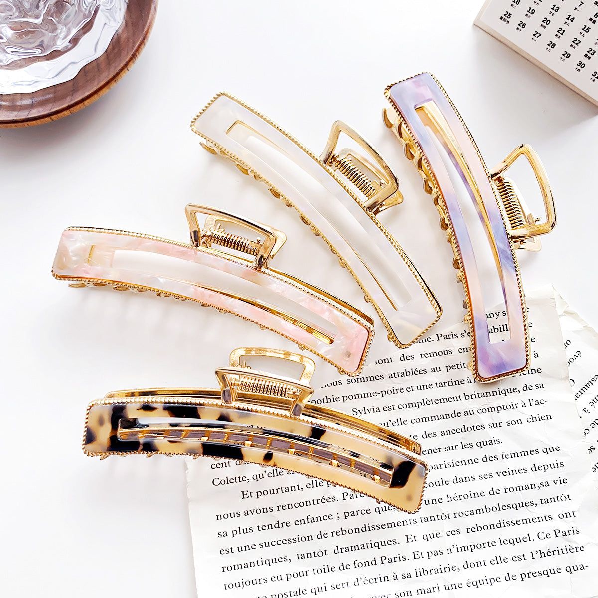 Una collezione di pinze per capelli in acetato da donna in vari colori come rosa, viola, bianco e tartaruga, tutte con una finitura in metallo dorato elegante.