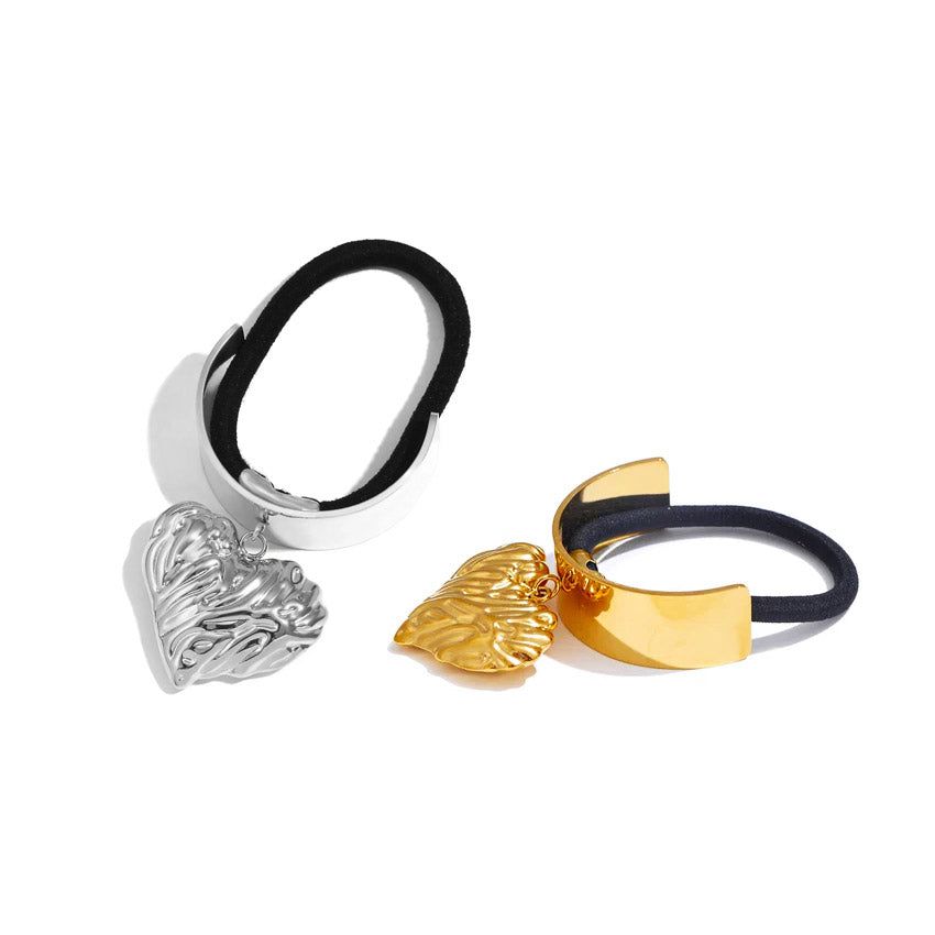 Ett par hårband i rostfritt stål med manschett för hästsvans, ett i guld och ett i silver, båda prydda med en stilren hjärtformad charm.