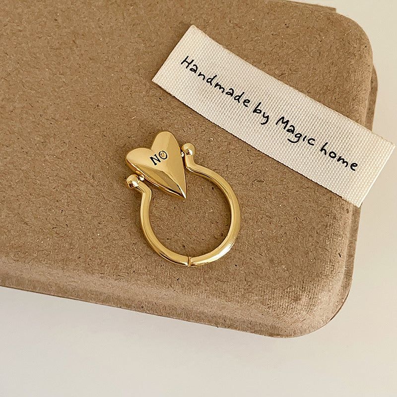 A collection of gold and silver plated brass rings with heart-shaped designs, engraved with 'YES' and 'NO', displayed on a neutral background.