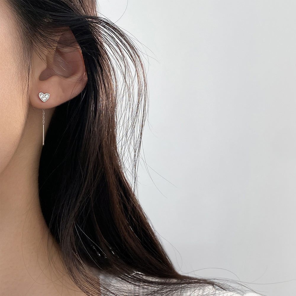 Un primo piano di una donna che indossa l'orecchino a filo a forma di cuore simmetrico vuoto in argento sterling 925 con zircon, che mette in mostra il suo design elegante.