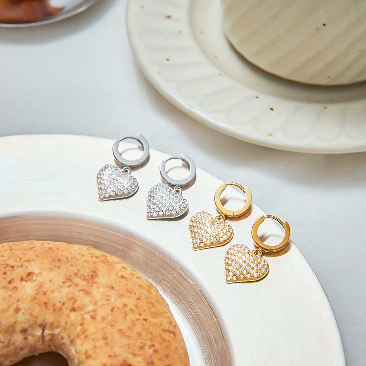 A display of Heart Zircon Hoop Earrings in both PVD gold plated and silver stainless steel, showcasing the sparkling heart-shaped charms on a clean white surface.