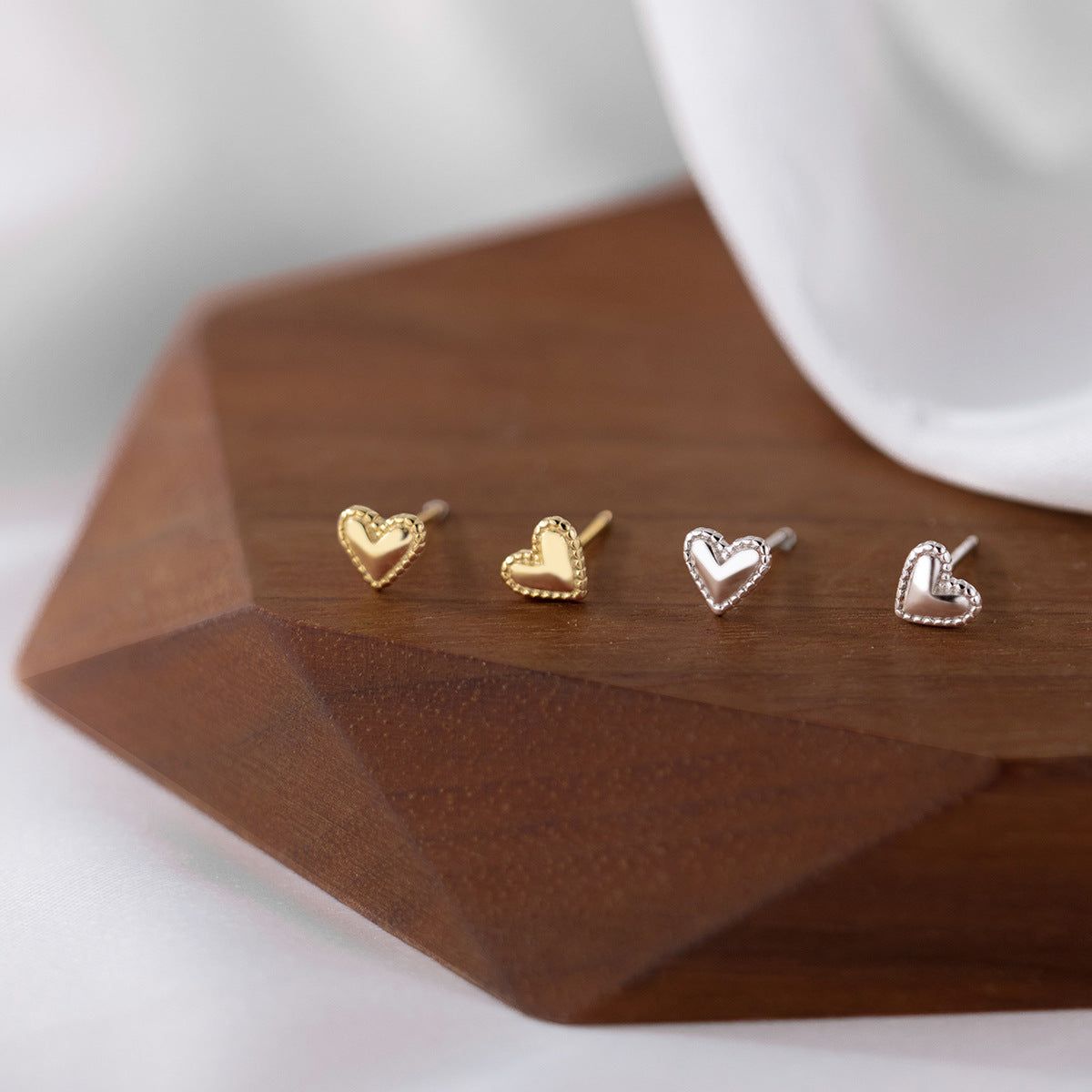 Un set di quattro orecchini a perno mini a forma di cuore in argento sterling 925, due in finitura argento lucido e due in finitura oro caldo, esposti su uno sfondo bianco pulito.