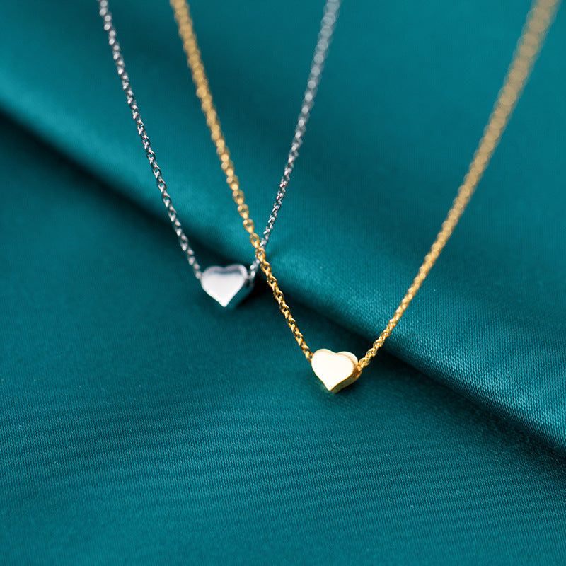 A set of 925 sterling silver tiny mini heart necklaces, with both gold and silver options elegantly displayed on a rich teal fabric.
