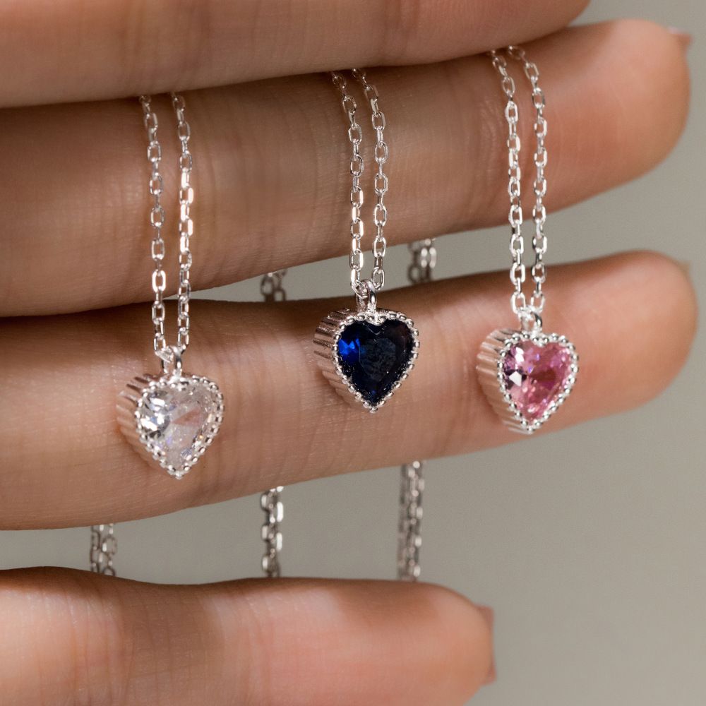 A collection of three 925 sterling silver heart necklaces featuring clear, blue, and pink CZ pave gemstones, displayed on a white background.