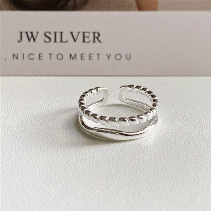 Un anneau ajustable à double bande en argent sterling 925 avec un design de chaîne torsadée unique, présenté sur un fond blanc propre.