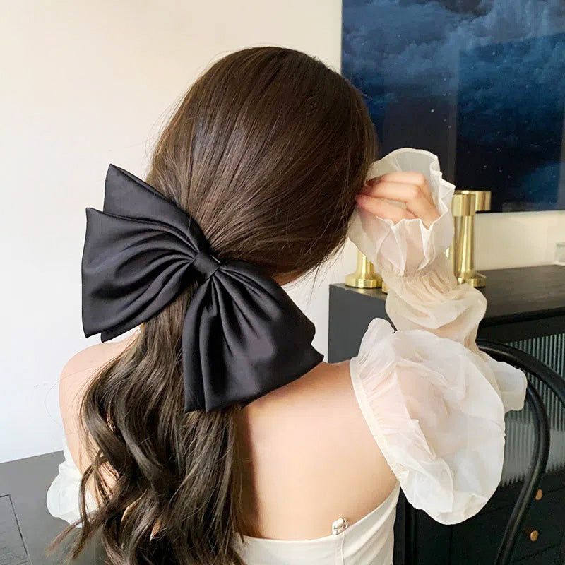 ダークヘアの女性が大きな黒の生地リボンボウのフレンチクリップを着用し、そのエレガントなスタイルを披露しています。