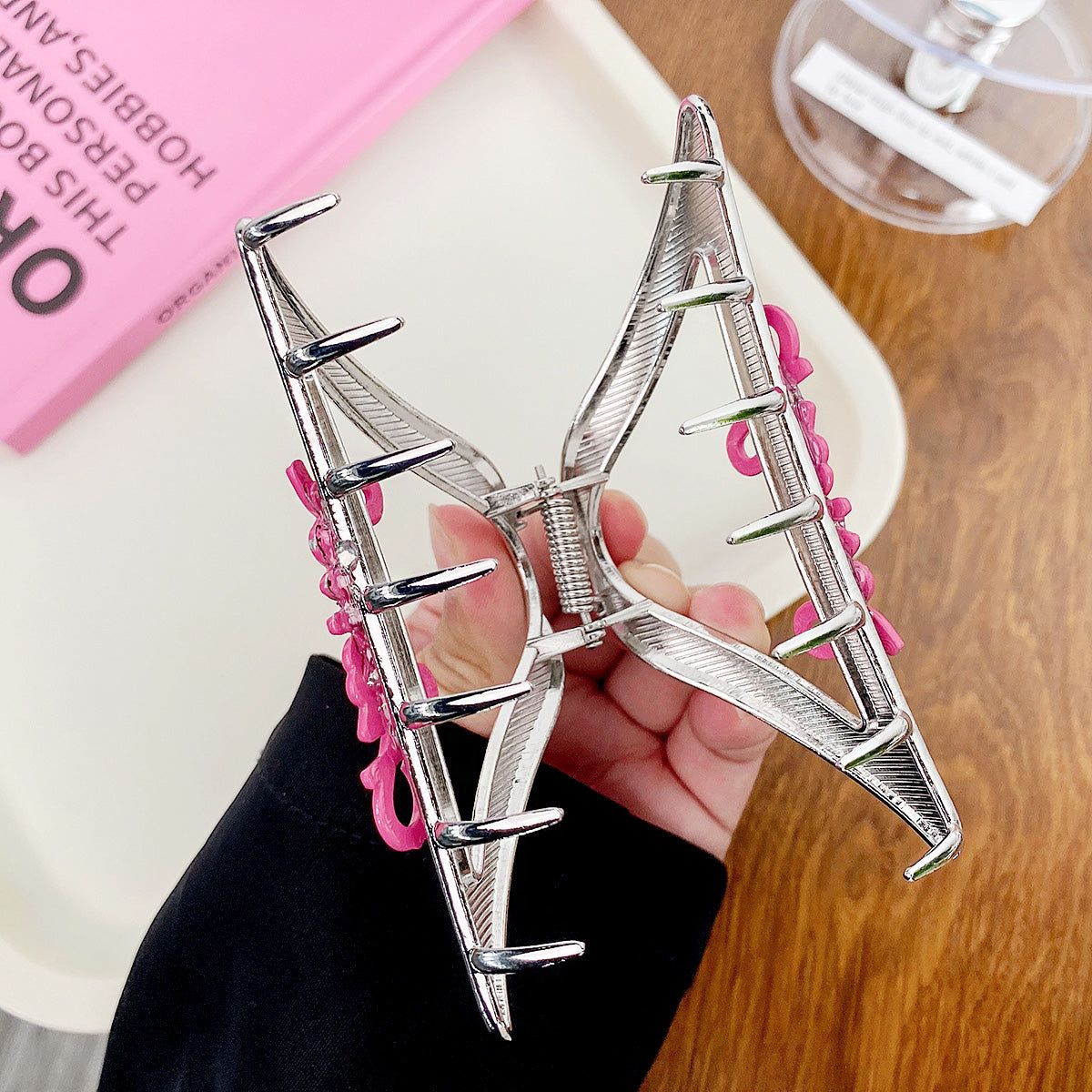 Een grote zilveren metalen haarclawclip in de vorm van een vlinder met roze accenten, vastgehouden in de hand om de grootte en details te tonen.