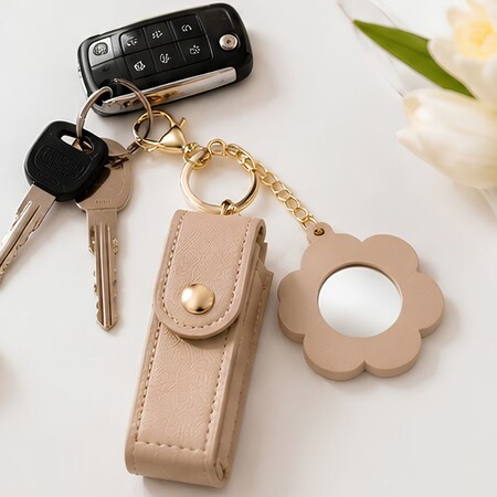 Beige leather lipstick holder keychain with flower-shaped mirror charm paired with car keys.