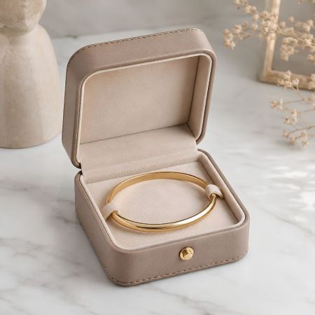 Taupe leren bangle doos met gouden sluiting met een gepolijste massief gouden bangle armband op fluwelen voering.