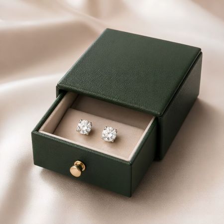 Donkergroene leren lade-stijl oorbeldoos half open met een paar schitterende ronde diamanten studs.