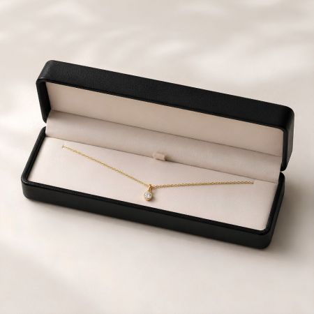 Lange zwarte leren kettingpresentatiedoos met een delicate gouden ketting met een solitaire pendant.