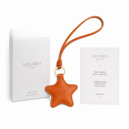 Orange star leather bag charm with debossed logo, branded white gift box, and matching insert thank you card.