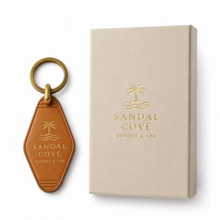 Llave de resort de cuero marrón con logo en foil dorado junto a un embalaje de caja de regalo premium a juego.