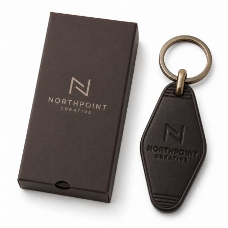 Llave de cuero corporativa marrón oscuro con logo grabado junto a una elegante caja de regalo deslizante.