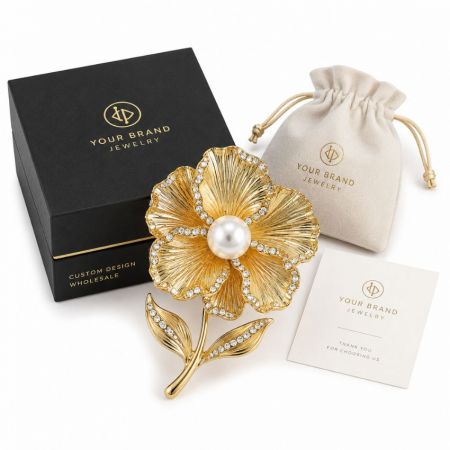 Wholesale custom design gold flower brooch with large central pearl, matching jewelry box, and velvet pouch.