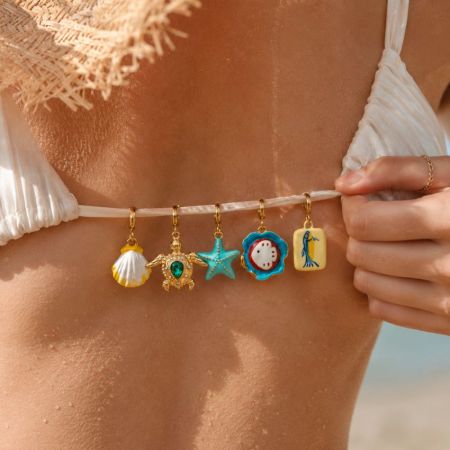 Gold plated enamel bikini charms arranged on a rock by the sea for premium swimwear brand sourcing.